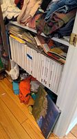 Photo showing shelf with white hardcover NASCAR books dated from 1991 to 2010, some magazines and papers above the books, and folded clothing nearby.