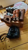 Overview of the Minolta body, Cintar camera with leather case, vintage binoculars, and Bushnell binoculars on the floor.