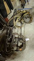 Photo showing multiple C-clamps, fabric tie-down straps, and metal tow chains lying on concrete floor.