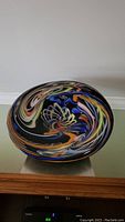 Front view of modern art style glass decorative plate showing colorful swirling patterns on black background.
