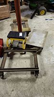 Four wheeled moving dollies and one yellow and black rolling stool grouped on concrete floor in basement. Items show usage wear and need cleaning.