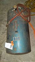 Full view of blue metal Grayson portable air tank model 404 with hose and pressure gauge lying on a concrete floor showing wear and rust.