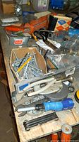 Close up of assorted nuts, bolts, clamps, and hand tools on a wooden surface showing mixed hardware and tools.