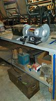 Wide view of workbench with Craftsman bench grinder, metal toolbox below, and various tools and supplies on and around the bench.