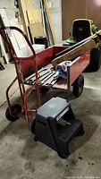 Red metal hand truck with step stool and various items stored inside