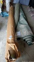 Rolled wool rugs and foam rug pad laid on floor, showing two rugs side by side with different covers and a rug pad between.