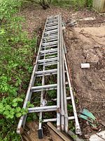 Two weathered aluminum extension ladders on grass and dirt, showing full length and close-up of ladder structure.