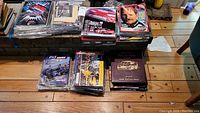 Stack of stock car themed magazines, some wrapped in plastic, and a black binder on a wooden floor.