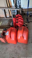 Three red plastic gas cans placed on a garage floor with four red motor oil containers behind them.