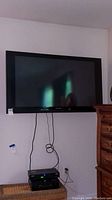 Panasonic 50-inch TV mounted on wall with cords hanging down and a device below it.