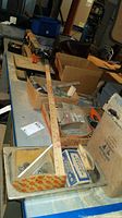 Photo showing a wooden yardstick placed on a metal tray along with several boxes containing bolts and small hardware parts on a workbench.
