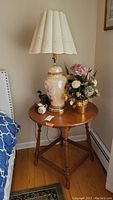 Wood round corner table with ceramic table lamp, faux flower arrangement, and small decorative items on top