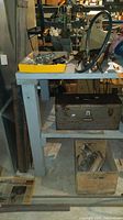 Workbench shelf with steel toolbox on middle shelf, assorted parts on top, and wooden crate below