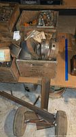 Wooden crates containing threaded pipes, metal clamps, and various metal parts on a basement floor.