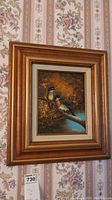 Framed painting of birds on branch with ornate golden frame hung on floral wallpaper
