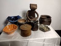 Artist made pottery pieces grouped and displayed on white cloth showing all items in clear daylight.