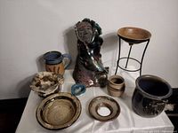 Full view of the multi-piece pottery lot including bowls, pitcher, small vase, figurative sculpture, and metal stand with clay bowl.