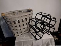 Woven basket with rope handles next to black metal wine rack on a white cloth