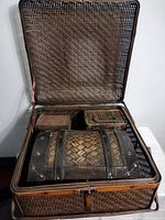 Photo of the interior of the large woven suitcase-style box with three smaller woven boxes inside, showing natural brown woven material and black metal bands.