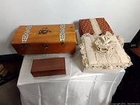 Three vintage boxes on a white cloth-covered table: wooden chest with metal accents and two decorative fabric-covered boxes