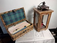 Wide view showing wooden lantern candle holder and wicker basket of taper candles on a table