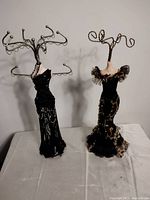 Front view of two dress form jewelry display stands on a white surface against a plain wall.