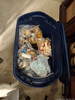 Blue plastic tote filled with plastic bags each containing a doll