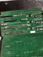 Overview photo of the complete drafting tool set inside its green velvet-lined black leather case showing compasses, extension bars, and drawing tools.