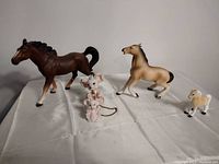 Photo showing two horse figurines and three small ceramic mouse figurines on white cloth surface.