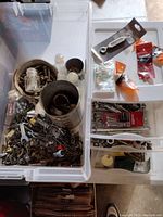 Wide view of white plastic tote filled with assorted hardware: screws, nails, hooks, washers, various small metal parts