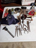 Tools arranged on a white table showing a variety of hand tools including pliers, caliper, compasses, hand drill, and Ryobi circular saw.