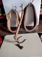 Two rustic leather horse collars positioned upright, leather is worn, one with frayed padding.