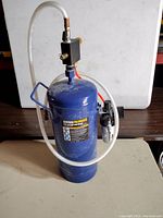 Full view of the blue soda blaster tank showing main body, white hose, and black tuner block on top with orange hose.