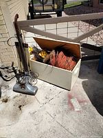 Vintage Kirby vacuum cleaner next to open wooden chest full of Halloween decorations on concrete floor outside next to a brick wall and metal gate.