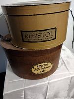 Two stacked vintage Resistol hat boxes, one tan and one brown textured, showing labels and handles.