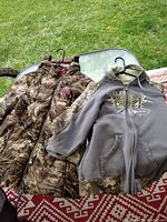 Two jackets on a chair outdoors, one camouflage and one gray with camouflage accents
