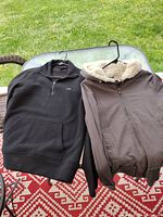 Two hoodies side by side, one black with a logo and half-zip, one brown with shearling collar