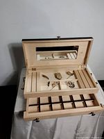 Open light wood jewelry box showing the box interior with compartments and a mirror, with vintage jewelry inside.