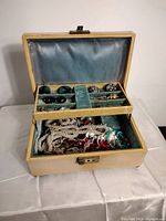 Wide view of vintage jewelry box open showing satin lined divided upper tray holding rings and earrings and lower compartment with assorted costume jewelry.