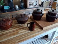 Photo showing all five Marcrest stoneware pieces arranged on a butcher block, including three crocks with lids, one bowl with lid, and small pitcher.