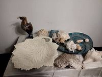 Lot of mixed decor items including platters, shells, coral pieces, and a glass eagle figurine arranged on a table.