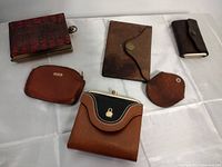 Photo of six vintage wallets and coin holders arranged on a white surface showing various materials, colors, and styles.