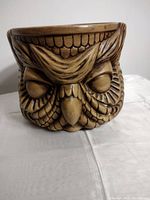 Front view of the brown owl-shaped container showing detailed carved feathers and facial features including closed eyes and a beak.