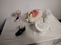 Overview of four ceramic pin cushions and one ceramic piggy bank displayed on a white cloth