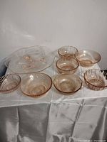 Photo showing all eight pink glass items including platter and bowls arranged on white fabric.