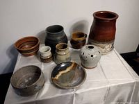 Overview photo showing all nine pottery pieces arranged on a white tablecloth including a tall vase, bowls, and small pots.