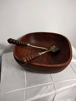 Vintage deep teak wood salad bowl with two vintage salad servers with wooden spiral handles and metal heads placed inside the bowl.