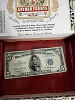 Five Dollar Silver Certificate lying on a red surface, showing the front with Abraham Lincoln portrait.