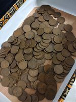 Photo showing a large number of wheat pennies spread out in a box, overlapping, copper color visible.