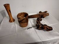 Photo shows four vintage wooden items on a white cloth: tall turned vase, barrel spout, wooden mortar, and corkscrew.